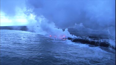 Where the edge of the Kilauea lava delta meets the ocean a line of steam rises into the air