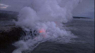 Where the edge of the Kilauea lava delta meets the ocean a line of steam rises into the air. Lava being washed out to sea.