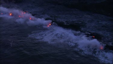 Where the edge of the Kilauea lava delta meets the ocean a line of steam rises into the air.