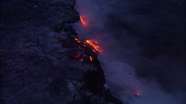 Where the edge of the Kilauea lava delta meets the ocean a line of steam rises into the air.