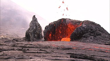 Lava bubbling through vents and flowing down channel. The lava is flowing beneath the solidified crust in lava tubes. Lava bubbles up and splashes. Eruption, erupting.