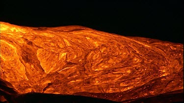 The molten rock incandescent lava moving across the surface. It looks plastic in form, soft and maleable as if it is being extruded. Bubbling out of the earth.