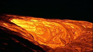 The molten rock incandescent lava moving across the surface. It looks plastic in form, soft and maleable as if it is being extruded. Bubbling out of the earth.