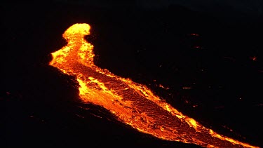 A river of incandescent lava flowing down a lava channel. Night