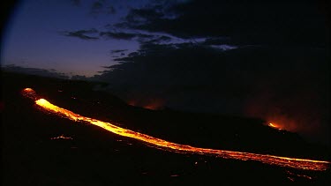 A river of incandescent lava flowing down a lava channel. Night