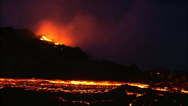 A river of incandescent lava flowing down a lava channel. Night