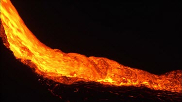 A river of incandescent lava flowing down a lava channel. Night