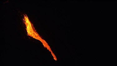 A river of incandescent lava flowing down a lava channel. Night