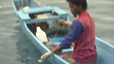 Fisherman pulling in a large orange fish on a blue sampan