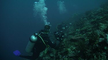 Pair of scuba divers with cameras on the edge of a reef