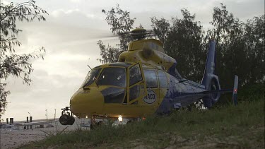 Yellow rescue helicopter on a beach with rotors spinning