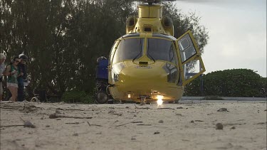 Yellow rescue helicopter on the beach with rotors spinning as baby Turtles crawl by