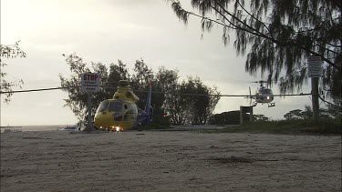 Yellow rescue helicopter on a beach with a white helicopter landing behind