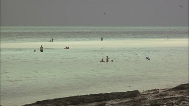 Families swimming in shallow water at the beach on a cloudy day