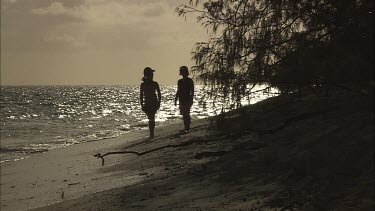 Two little girls walking along the beach. Sunset