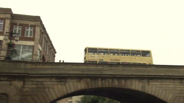 Double decker bus traveling over a stone bridge in a city