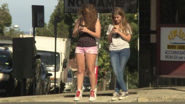 Friends texting on their smartphones on a street corner