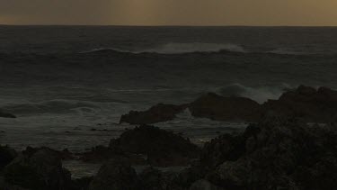 Waves breaking against a rocky shore at sunset