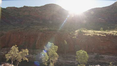 Bright sunlight streaming over a rocky cliff and river