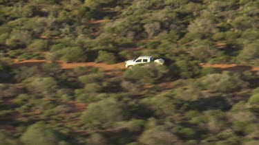 White truck driving a dirt road through desert vegetation