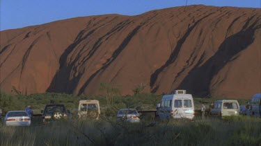 pan across Uluru with line up of tourist vehicles in foreground small hair in gate at top