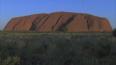 Uluru with low vegetation in foreground entire monolith in shot small hair in gate at top