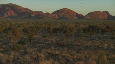 pan around Kata Juta rock formations being and vegetation in foreground small hair in gate top right