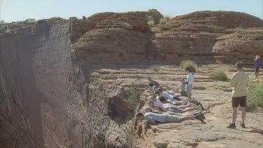 pull out from tourists lying down on edge of steep cliff looking over edge into deep gorge