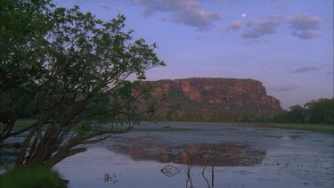 Nourlangie Rock and escarpment from Nawurlandja Lookout vista with water in foreground and reflection of rock in water *