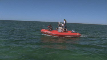 marine scientists on red zodiac inflatable boat heading out across bay
