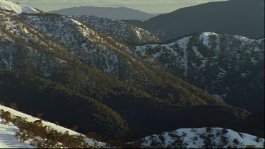 early morning light over snow covered valleys wooded with snow gums then pan up to snow covered peaks