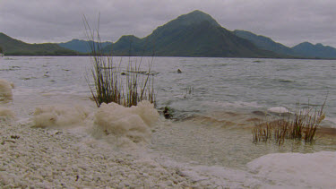 Foam at shore of celery top island in foreground with Bathurst Harbor and mountains behind