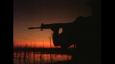 Loading, aiming and pulling trigger of rifle, silhouette against red sky.