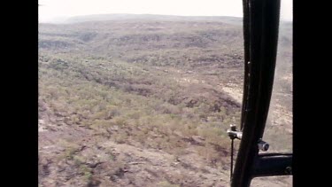 Track through interior of helicopter window looking down on dry savannah