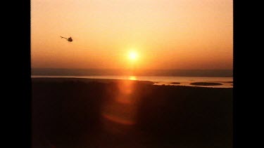 Sunset. A helicopter flies against the orange sky over a meandering river