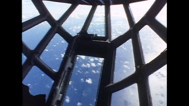Sky through nose window of cargo plane, see small cumulus clouds dotting sky below