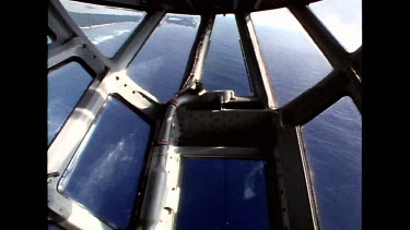 Sky through nose window of cargo plane, see sand and sea below