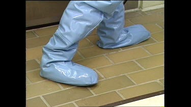Man in chemical suit puts on special rubber shoes