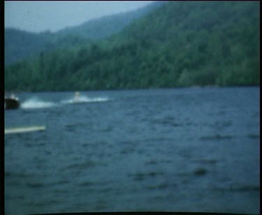 Man on waterskis passes other boys waiting on the pier and falls off