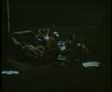 Group of men relaxing by the lake on grass in low light