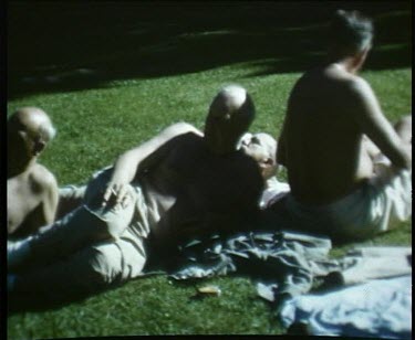 Topless men converse and relax in the sun on the grass