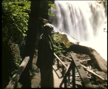 man on bridge walkway watches waterfall