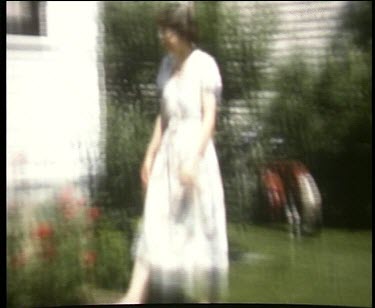 Woman in white dress walks through garden and picks at flowers