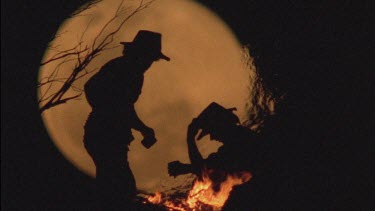 men sitting around campfire, huge moon in background