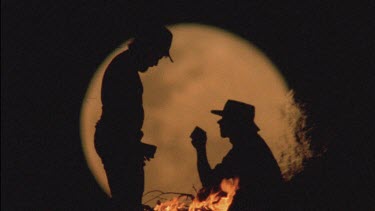 silhouette men drinking around campfire, huge moon in background