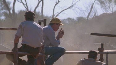 men sitting on gate, one is smoking, CU to smoking guy