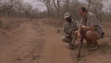 scientist Andrew Parker and Tracker Elias Mathabula on roadside looking down at tracks then walk away