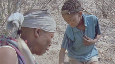 bushman woman digging for poison arrow worms , little boy helping dig away soil
