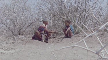 bushman woman and little boy picking out beetle larvae for poison arrow , little boy runs out of shot