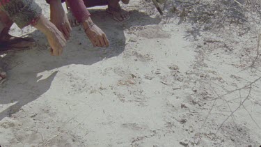 Bushman pointing to tracks in earth with fingers then stand up and walk out of shot